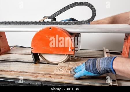 Un lavoratore sta tagliando una piastrella ceramica su una macchina di taglio a umido. Foto Stock