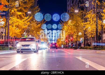 30 Novembre 2019 - Granada, Spagna. Auto su una strada a tre corsie in Calle Gran Via de Colón. Ornamenti di Natale appesi sulla strada e alberi con voi Foto Stock