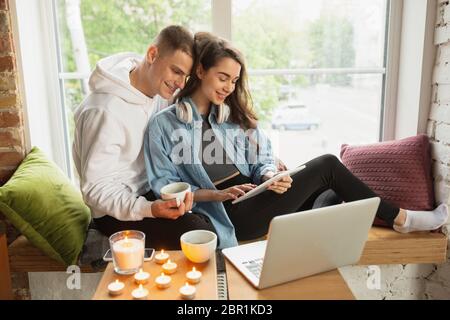 Bere tè, guardare il cinema, guardare felice. Quarantena lockdown, soggiorno casa concetto - giovane bella coppia caucasica godendo di nuovo stile di vita durante coronavirus. Felicità, togetherness, sanità. Foto Stock