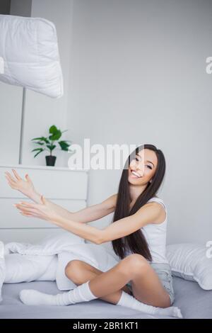 Buongiorno. Ritratto di una giovane donna bruna sorridente che si rilassa nel letto bianco Foto Stock
