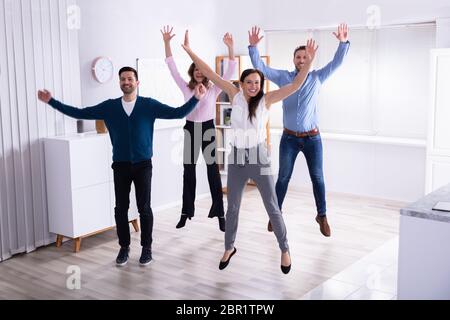 Giovani Imprenditori Jumping in Office alzando le braccia Foto Stock