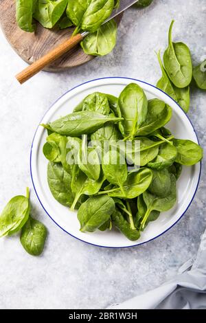 Foglie di spinaci in ciotola su fondo grigio in cemento, vista dall'alto, spazio copia. Cibo pulito, detox, dieta ingrediente alimentare Foto Stock