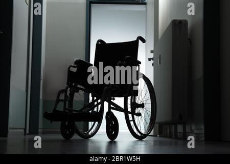 Silhouette di sedia a rotelle vuota parcheggiata nel corridoio di ospedale Foto Stock