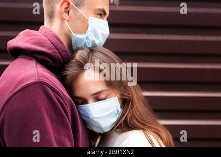 Giovane coppia spaventata abbracciando una maschera di protezione del viso in città dal nuovo Coronavirus Covid 19 Foto Stock