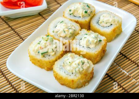 Involtini di sushi tempura Maki con formaggio cremoso, su un piatto bianco da vicino. Rotolo di granchio fritto Foto Stock