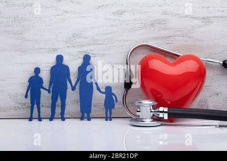 Close-up di una famiglia con uno stetoscopio e cuore rosso forma nella parte anteriore della parete in legno Foto Stock