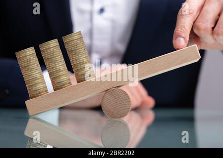 Imprenditore di bilanciamento delle monete impilate con il dito sull'altalena in legno sulla scrivania riflettente Foto Stock