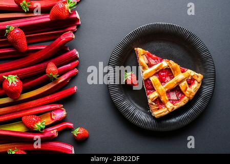 Una fetta di torta fatta con rabarbaro e fragole. Fetta di torta di frutta su un piatto nero, vista dall'alto. Foto Stock