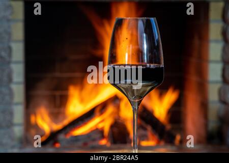 Un bicchiere di vino rosso prima di accogliente camino in casa di campagna, vacanze. Foto Stock