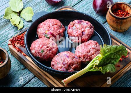 Polpettine di carne di manzo crudo forza-carni in ghisa pan Foto Stock