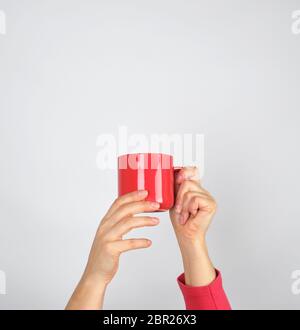 Mani femminili tenere un rosso tazza di ceramica e sfondo grigio Foto Stock