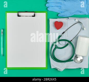 Titolare della carta con vuoto fogli bianchi, medico stetoscopio, pillole su uno sfondo verde, vista dall'alto, lo spazio per la scrittura di una prescrizione Foto Stock