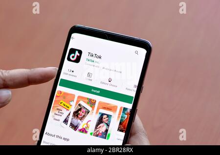 Delhi, India, 2020. Donna che installa l'app mobile TikTok su uno schermo per smartphone con uno sfondo in legno raffigurante il logo di popolari social in rapida crescita Foto Stock