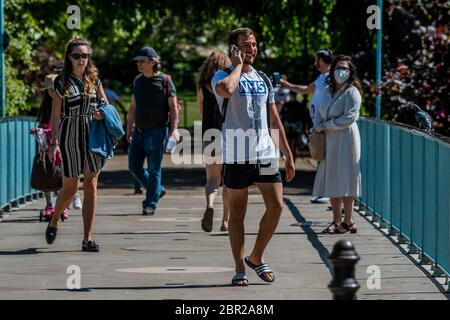 Londra, Regno Unito. 20 Maggio 2020. Ci sono ancora alcuni turisti e un uomo e NHS ha ottenuto la mia maglietta posteriore sul ponte - alcune maschere di wwear, la maggior parte non. Godendo il sole nel parco di St James mentre il sole esce di nuovo. Il "blocco" continua per l'epidemia di Coronavirus (Covid 19) a Londra. Credit: Guy Bell/Alamy Live News Foto Stock