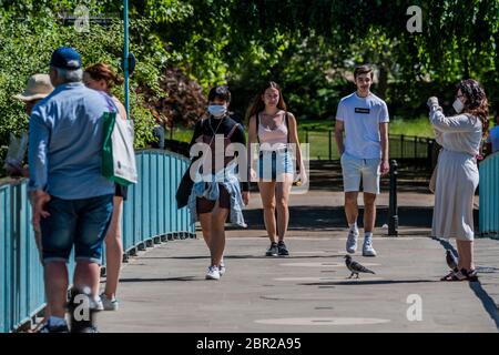 Londra, Regno Unito. 20 Maggio 2020. Ci sono ancora alcuni turisti sul ponte - alcune maschere di wwear, la maggior parte non. Godendo il sole nel parco di St James mentre il sole esce di nuovo. Il "blocco" continua per l'epidemia di Coronavirus (Covid 19) a Londra. Credit: Guy Bell/Alamy Live News Foto Stock