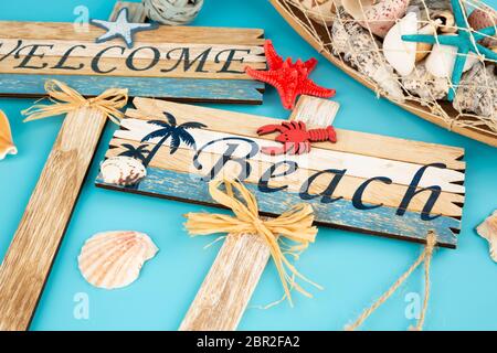 Cartelli in legno danno il benvenuto alla spiaggia e alle conchiglie su sfondo blu. Foto Stock