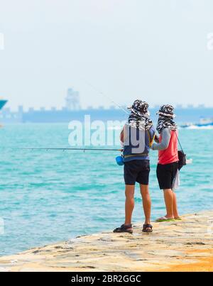 I pescatori pesca dalla diga del porto di Singapore. Commerciale di navi da carico in background Foto Stock