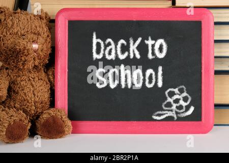 Brown orsacchiotto e lavagna nera con cornice rossa sullo sfondo della pila di libri, concetto si torna a scuola Foto Stock