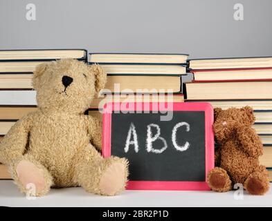 Brown orsacchiotto e lavagna nera con cornice rossa sullo sfondo della pila di libri, concetto si torna a scuola Foto Stock