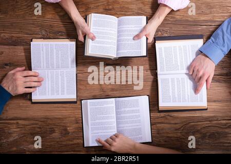 Una vista in elevato di persone che leggono libri santi su sfondo di legno Foto Stock