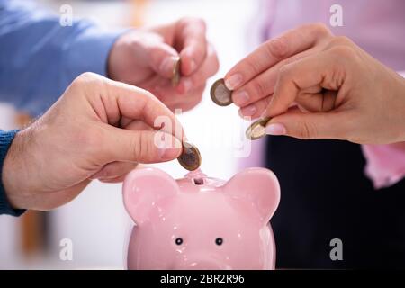 Gli imprenditori di mano inserire monete in rosa Piggybank in Office Foto Stock