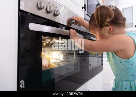 Bambina giocando con il sistema elettrico di un forno a microonde in cucina Foto Stock