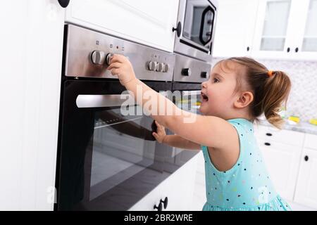 Bambina giocando con il sistema elettrico di un forno a microonde in cucina Foto Stock