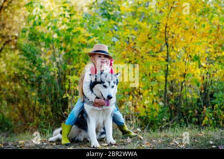 Ragazza in cappello abbracciando il suo cane. Bambina con il suo cane, malamuta alaska, lunghezza intera. Bambino e cane su sfondo natura. Infanzia spensierata. Natura w Foto Stock