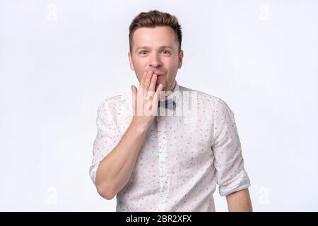 Sorprende il giovane bell'uomo che ricopre la bocca con la mano e fissando la fotocamera con shock. Scatto in studio Foto Stock