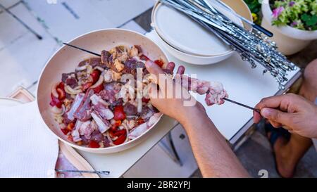 Le mani di un uomo di mettere carne su spiedini per barbecue. Close-up immagine della carne cruda su spiedino. Foto Stock