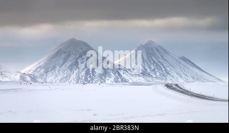 Twin neve coperta di sole cime vulcaniche vicino al Lago Myvatn, Islanda del Nord con strada in inverno Foto Stock