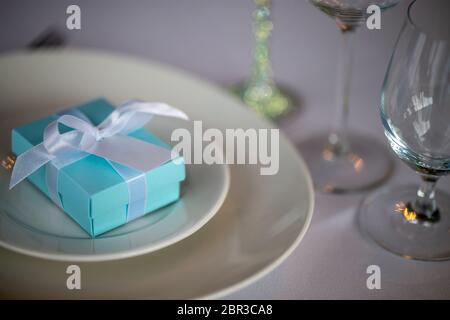 Festosa messa in tavola con fatti a mano scatola regalo sulla piastra. Luce blu a mano confezione regalo nella piastra sulla tabella di nozze. Foto Stock