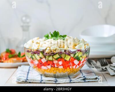 Grande recipiente di vetro con insalata di granchio, mais, cetriolo e riso a tavola. Bastoncini di granchio e insalata di mais. Insalata di maionese tradizionale per holi russi Foto Stock