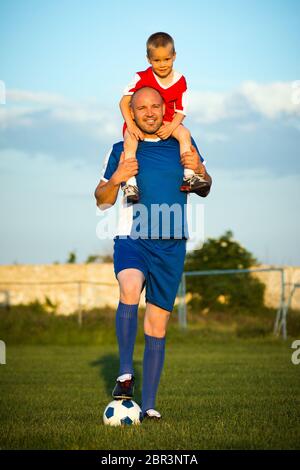 Il padre e il figlio felici della famiglia gioca a calcio all'aperto sul campo da gioco di erba verde sul campo da gioco di calcio. Foto Stock