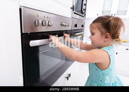 Bambina giocando con il sistema elettrico di un forno a microonde in cucina Foto Stock