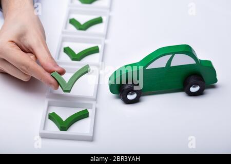 Mano umana ponendo icona con il segno di spunta accanto a piccoli verde auto Foto Stock