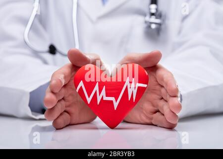 Close-up di maschio del medico di protezione mano cuore rosso forma con bianco di impulsi del battito Foto Stock