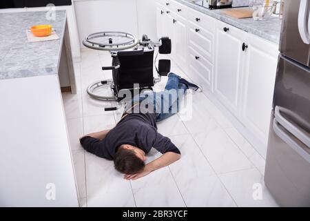 Disabilitato uomo disteso in cucina dopo aver sceso dalla sedia a rotelle Foto Stock