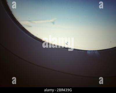 Finestra di un aereo con un piccolo foro per regolare la pressione tra i finestrini esterni e interni. Cielo chiaro e l'ala sullo sfondo. SA Foto Stock