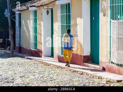 Un uomo cammina lungo un marciapiede a Trinidad, Cuba un pomeriggio verso il sole tramontare nel novembre 2015. Foto Stock