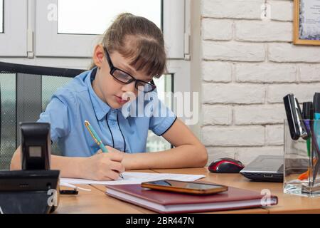 Un otto-anno-vecchia ragazza al tavolo in ufficio scrive una penna stilografica su un pezzo di carta Foto Stock