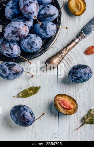 Susine mature con spicchi di frutta, foglie e vintage lama di luce su una superficie di legno. Vista da sopra Foto Stock