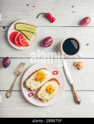 La colazione brinda con verdure e uova fritte su piastra bianca, una tazza di caffè e un po' di frutta su sfondo di legno. Pulire a mangiare cibo concetto. Visualizza f Foto Stock