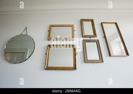 Basso angolo vista di un muro di una casa che ha una varietà di diversi specchi sagomati appesi al muro. Foto Stock