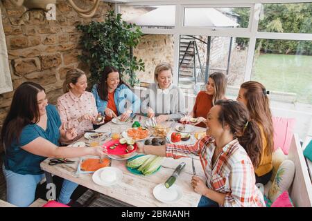 Piccolo gruppo di amici di sesso femminile con un misto di età seduti ad un tavolo che preparano la loro cena. Foto Stock