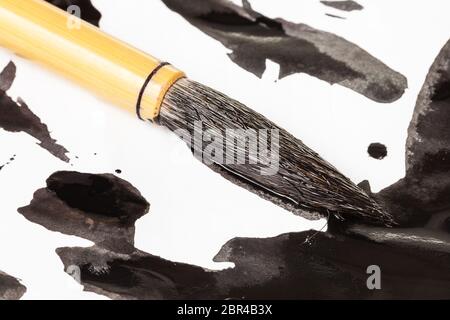 Tinto nero round pelo di capra punta del pennello di bambù per sumi-e ( suibokuga) pittura su macchie di inchiostro sulla carta bianca close up Foto Stock