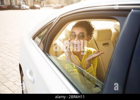 Gioiosa Signora Africana che parla sul telefono cellulare seduto in auto Foto Stock