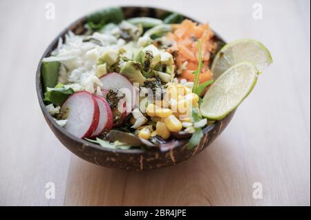Insalata vegana deliziosa e sana con mais, lattuga, rafano, carote e condimento serviti nella ciotola di buddha di cocco. Foto Stock