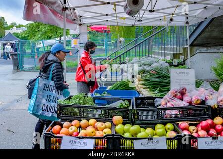 Donna che indossa la maschera, durante i negozi epidemici di Covid-19 per i verdi freschi al mercato agricolo di Kitsilano, Vancouver, British Columbia, Canada Foto Stock