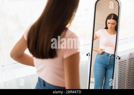 Donna infelice che guadagna peso toccando il ventoso che si trova a Specchio in interni Foto Stock